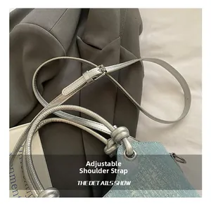 Detail of adjustable silver shoulder strap on a light blue denim crossbody bucket bag