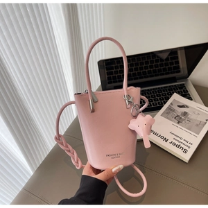 Pink leather bucket bag with woven strap and elephant charm on a modern desk setup