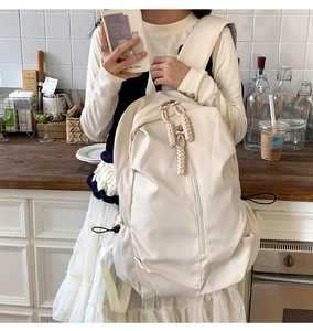 Detail of cream backpack with braided zipper pulls and side drawstring pockets
