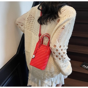 Détail du sac seau tressé rouge montrant la texture fine, le pendentif et la bandoulière