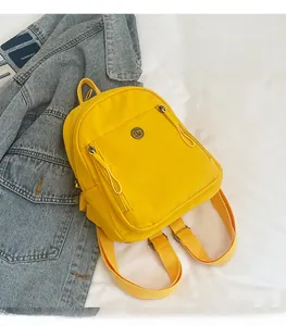 Detailansicht des gelben Nylon-Minirucksacks mit doppelten Reißverschlusstaschen und Metalllogo