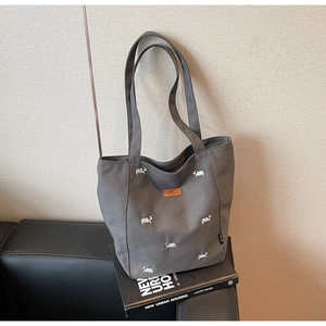 Detail of embroidered colorful dog patterns on gray canvas tote bag over a magazine
