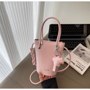 Close-up of pink leather bucket bag with elephant charm and woven strap on a desk