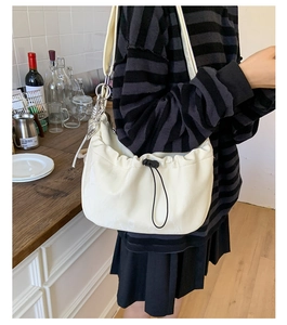 Detail of a beige cloud bag with pleated drawstring design and metallic chain shoulder strap