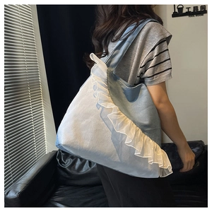 Detailed view of large denim tote bag featuring white ruffled lace trim and wide shoulder strap