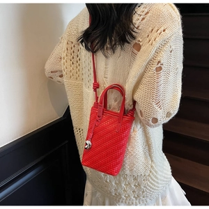 Gros plan détaillé d'un mini sac seau tressé rouge avec poignées en cuir et pendentif
