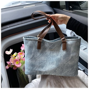 Detail of blue textured tote bag with brown leather handles and gold metal ring connectors