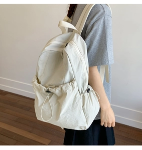 Detail of minimalist cream nylon backpack showing drawstring pocket and adjustable straps