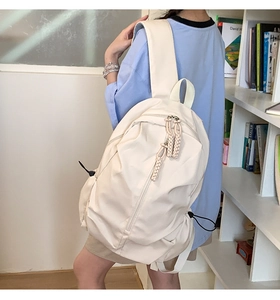 Side view of cream white nylon backpack with decorative braided zipper pulls on a model