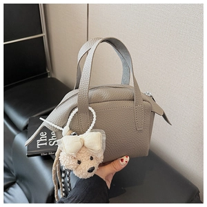 Détail d'un sac à main gris avec texture grainée et un pendentif ours en peluche