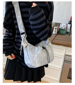 Detail of silver metallic textured bag with black drawstring and heart charm on wide strap