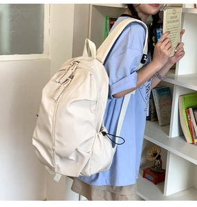 Detail of beige nylon backpack with double zippers and drawstring side pockets in library