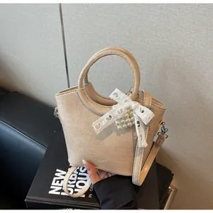 Close-up of beige crocodile-embossed handbag with pearl charms and lace bow details