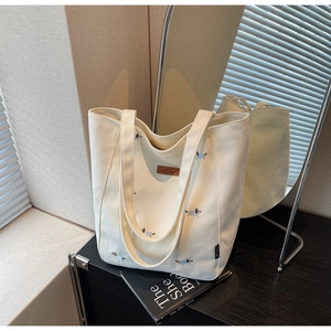 Detail of embroidered dachshund patterns and leather logo on white canvas tote bag