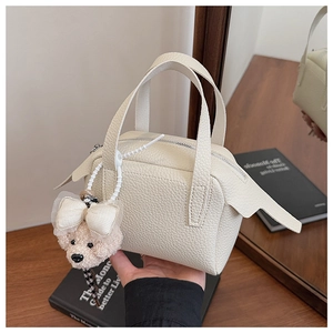 Gros plan d'un sac à main minimaliste en cuir crème avec pendentif ours et nœud