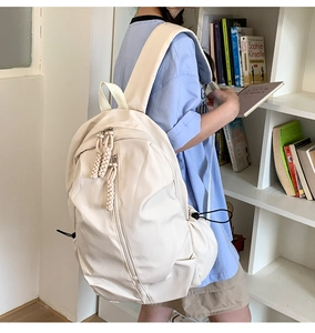 Detail view of cream white nylon backpack featuring woven rope zippers and side drawstrings