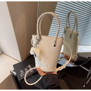Detail view of cream leather bucket bag featuring a cute elephant charm and rope strap