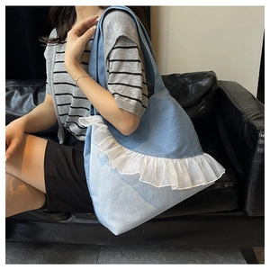 Close-up of light blue denim tote bag with white lace trim and wide shoulder strap
