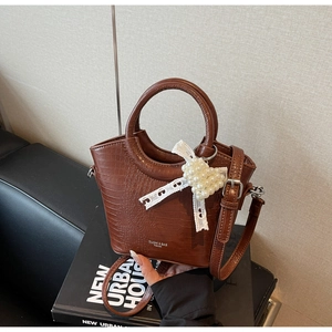 Detail of brown crocodile pattern handbag with pearl bow charm and logo branding
