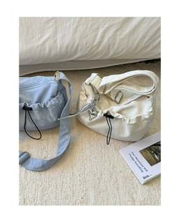 Detail view of ruched crescent crossbody bags in blue and cream on a soft white carpet