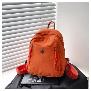 Détail d'un sac à dos en nylon orange vif avec plusieurs poches et logo en métal