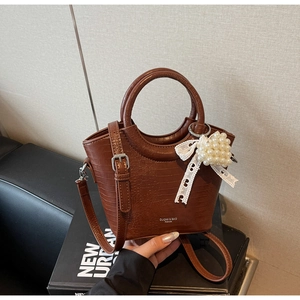 Detail of brown crocodile pattern bucket bag with pearl heart charm and lace bow
