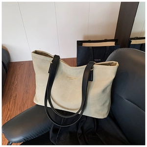 Chic tote bag detail showing black leather handles and golden fashion text on beige surface