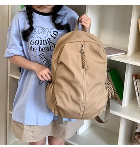 Detail view of khaki nylon backpack with vertical zipper and woven decorative cord puller