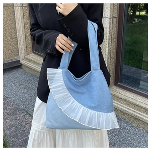 Close-up of light blue denim tote bag with white chiffon ruffle details and shoulder strap