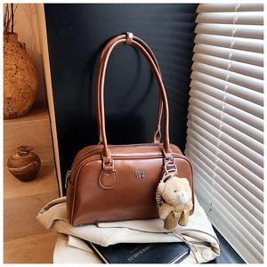 Gros plan du sac bandoulière en cuir marron avec charm ours en peluche et logo en métal