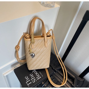 Détail du sac seau tressé beige avec breloque cœur argentée et bandoulière nouée