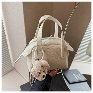 Détail d'un sac à main en cuir crème à grain lychee avec un pendentif ours en peluche