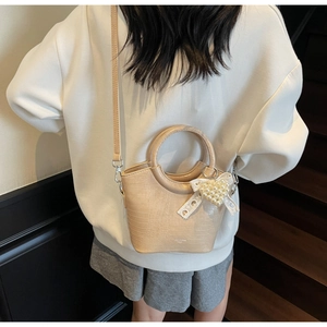 Detail of a beige crocodile pattern bucket bag with pearl heart and lace bow