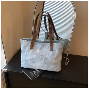 Detail of blue washed canvas tote with leather handles and gold lettering