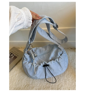 Close-up of light blue pleated dumpling bag with drawstring and silver spiral pendant