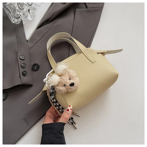 Détail d'un mini sac à main beige en cuir grainé avec un pendentif ours en peluche