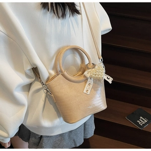 Detail of cream mini bucket bag featuring crocodile pattern leather and pearl heart charm