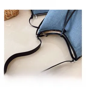 Close-up of denim tote bag showing leather strap stitching and metal zipper hardware