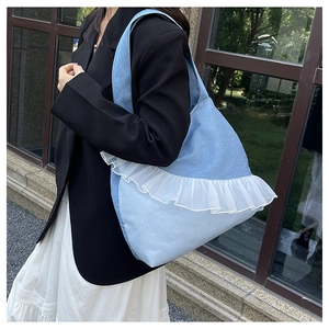 Detail of light blue denim tote bag featuring elegant white lace ruffle and sturdy shoulder strap
