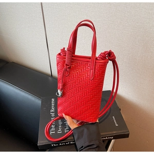 Détail du sac seau tressé rouge avec pendentif oiseau argenté sur un livre noir