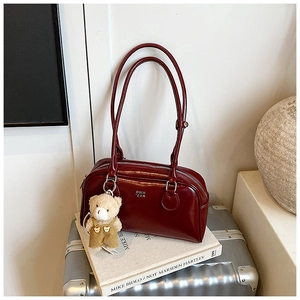Dettaglio della borsa Boston bordeaux in pelle lucida con ciondolo a orso e tracolla