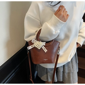 Detail of brown crocodile pattern bucket bag featuring a pearl lace bow and logo