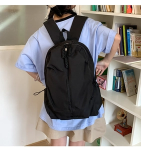 Detail of black nylon backpack with woven zipper and drawstring side pockets on the model