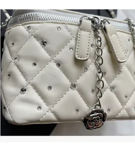 Detail of white quilted handbag with crystal studs and rose metal charm on silver chain