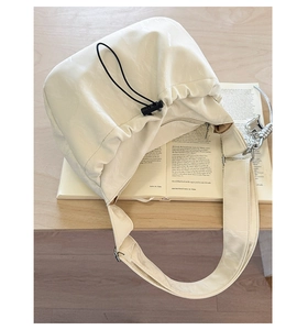 Detail of cream drawstring pleated bag showing glossy soft leather and silver ornament