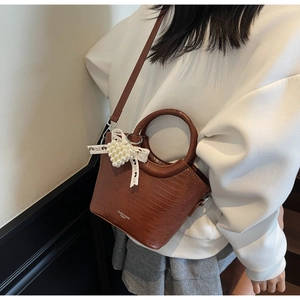 Detail of brown crocodile pattern handbag with pearl lace bow and metal ring handle