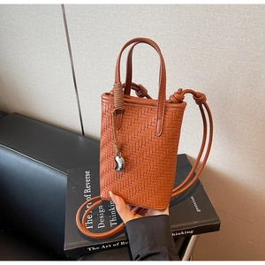 Détail d'un mini sac cabas tressé marron avec poignées nouées et breloque argentée