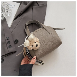 Détail d'un mini sac à main gris en cuir avec pendentif ours sur fond de blazer gris foncé