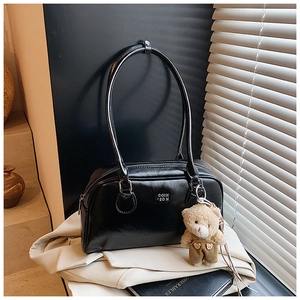 Détail du sac à bandoulière en cuir verni noir avec un petit ours en peluche marron