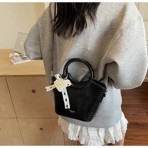 Detail of black croc-textured bucket bag with white lace bow and pearl heart charm